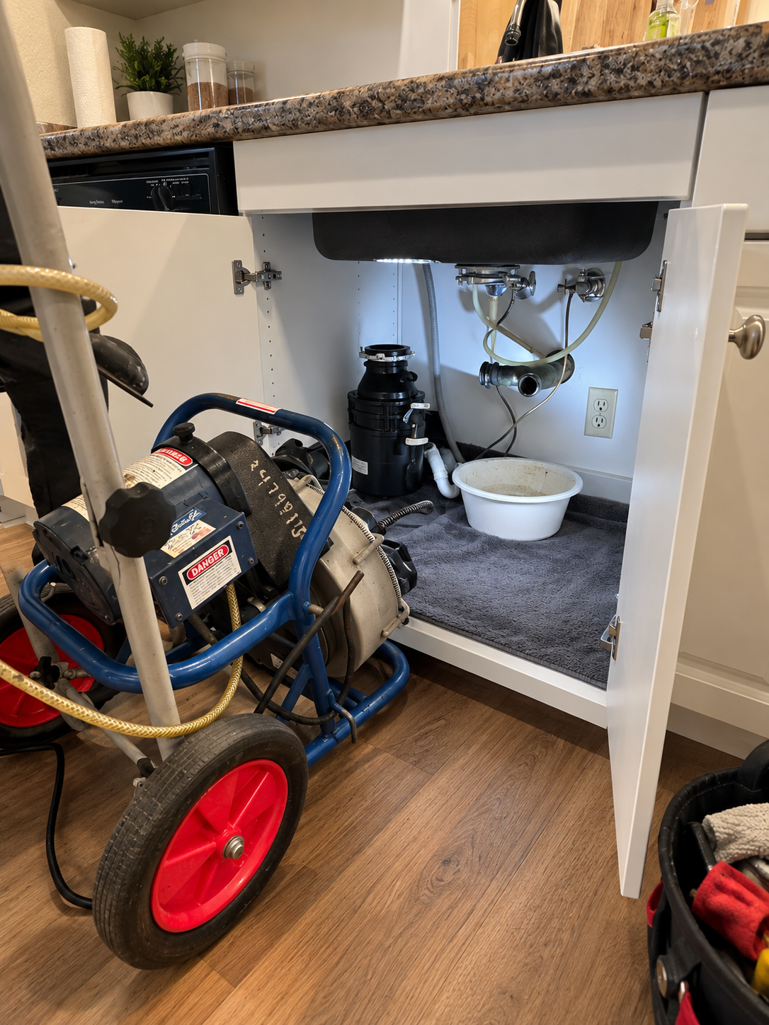 Professional drain-clearing equipment beside an open kitchen sink cabinet