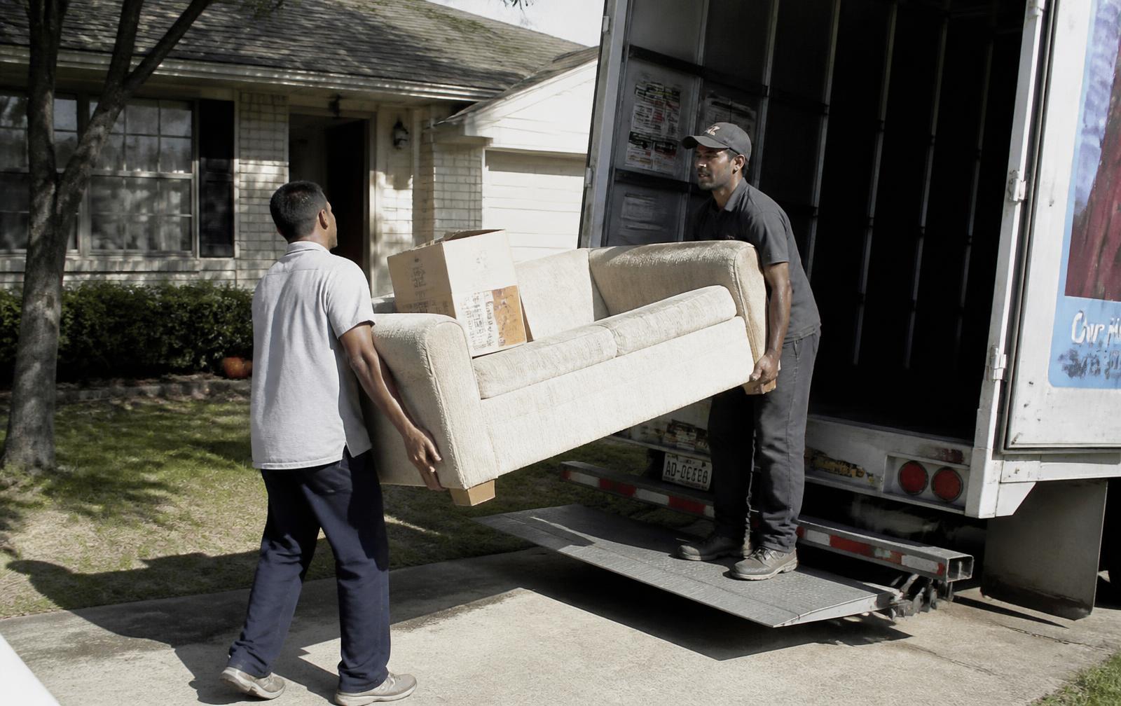 Two workers carrying an old couch out of a home into a box truck
